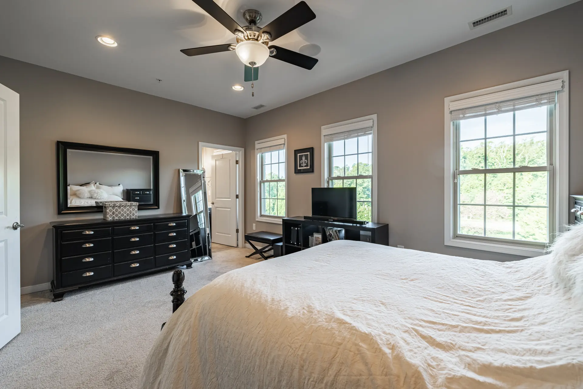 Bedroom with ceiling fan, dresser and three windows