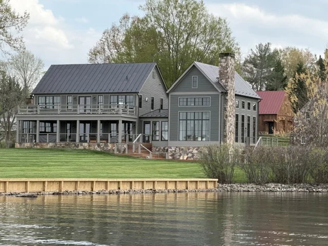 Gray waterfront home with stone chimney, covered porches and a wood seawall in Lake Anna, Virginia